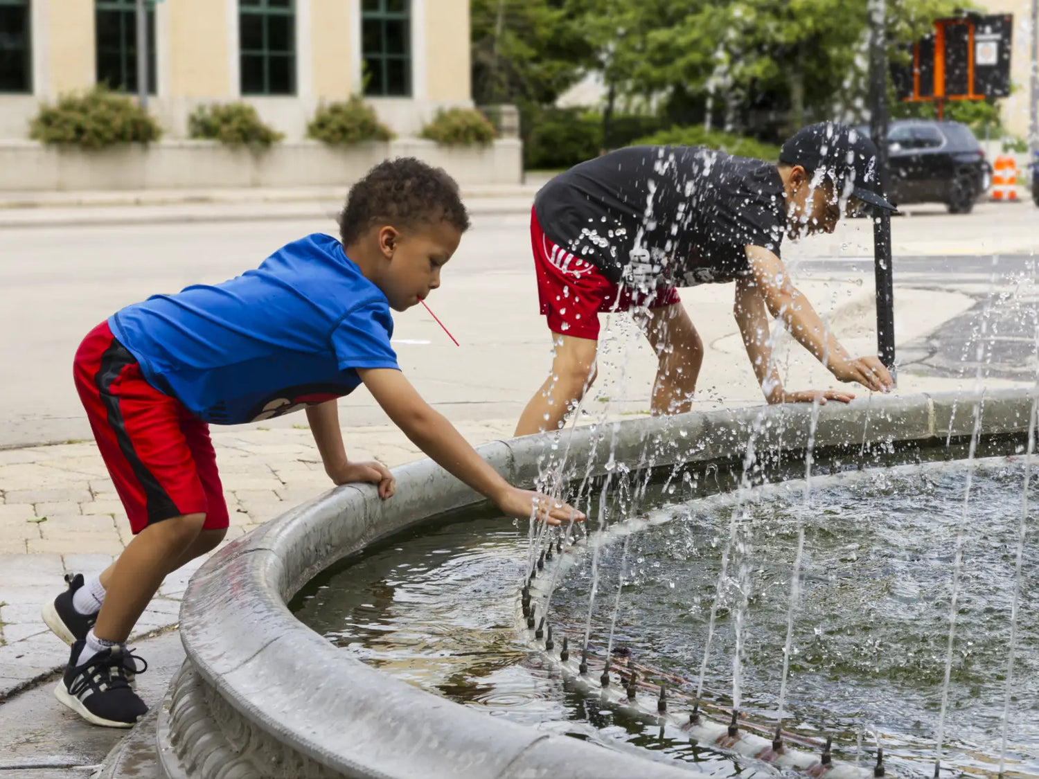 Two boys playing in a downtown fountain during a summer outing with their dad.