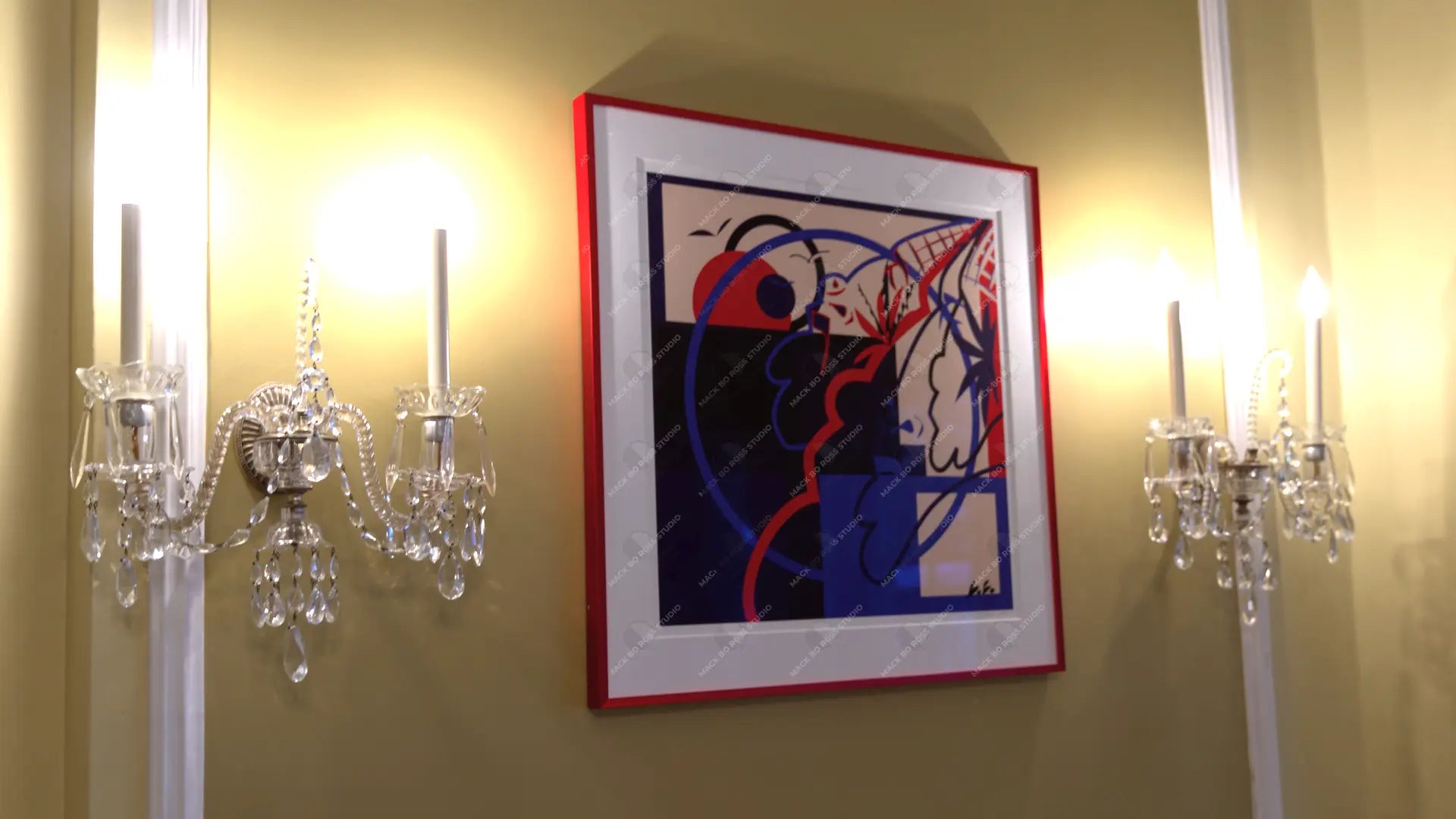 Framed abstract artwork on a wall with two crystal candelabras.
