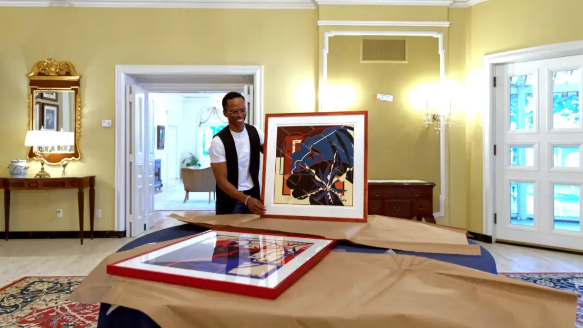 Person standing in a room with framed artwork on a table
