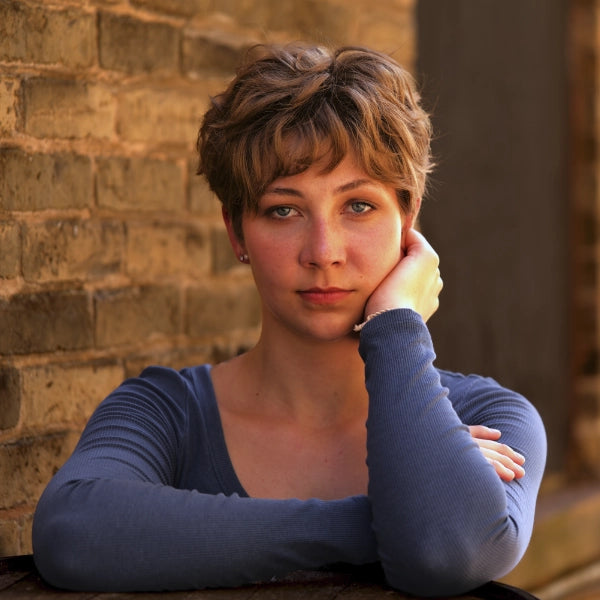 Woman with short hair resting her head on her hand against a brick wall.